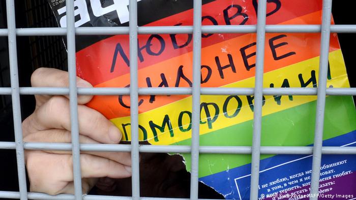 A man from behind bars shows a poster in rainbow colors